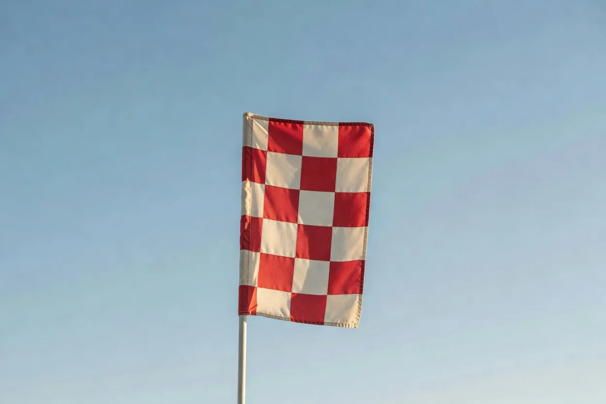 A plain checkered assistant referee flag raised against a bright sky
